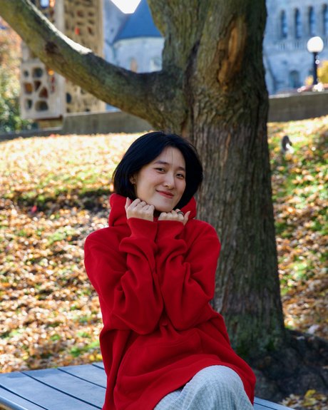 Ziyi (Ellen) Zhou in a red sweater, sitting under a tree among autumn leaves